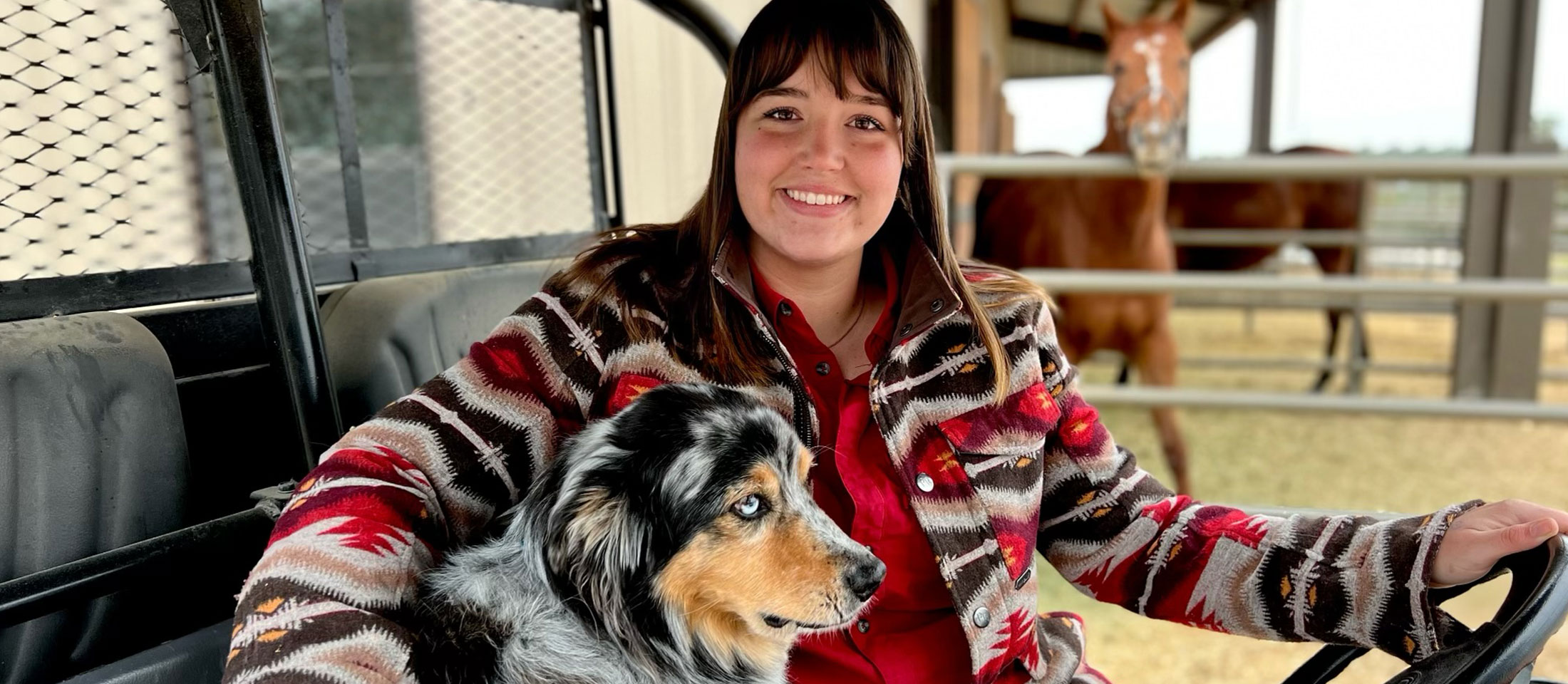 Abby driving a side by side while petting her dog. Horses are in the background.